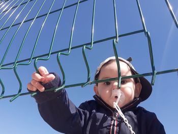 Low angle portrait of baby boy with pacifier in mouth standing by fence