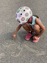 Little girl with a helmet draws on the floor sand 