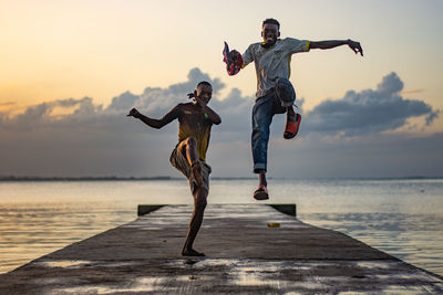 Full length of two men jumping on beach against sky during sunset