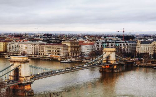 Bridge over river in city against cloudy sky