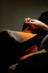 Midsection of woman knitting while sitting against gray background