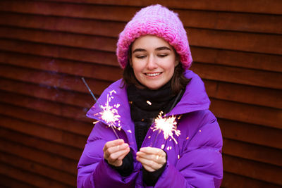 Happy young woman in outerwear with sparklers on the street on the background