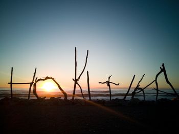 Silhouette wooden posts on beach against clear sky during sunset