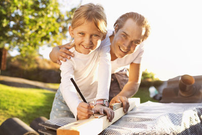 Portrait of happy father assisting daughter in measuring plank