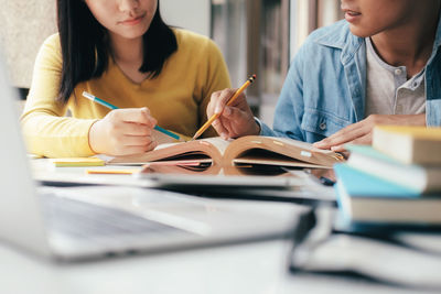 Midsection of friends reading book while sitting at table