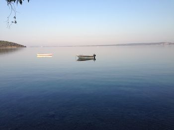 Boats in calm sea against clear sky