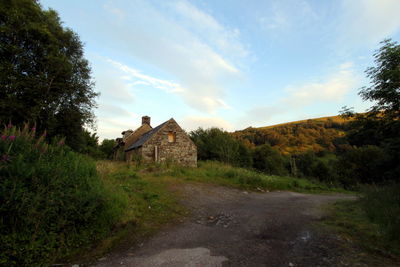 House and trees by footpath against sky