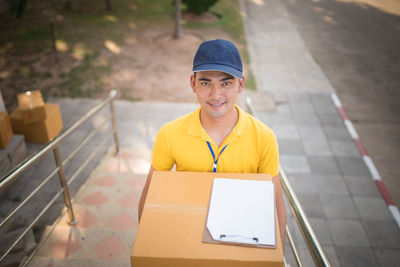 Portrait of smiling delivery man with package and clipboard standing at footpath 