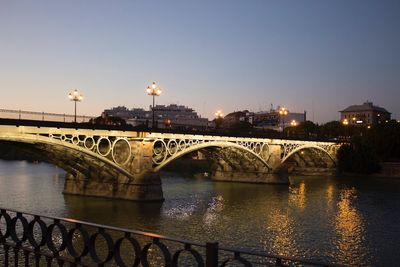 Bridge over river in city against clear sky at night