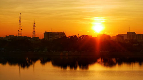 Silhouette buildings by river against sky during sunset