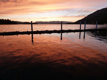 Silhouette wooden posts in sea against orange sky