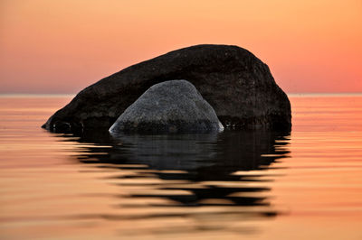 Rock formation in sea against sky during sunset