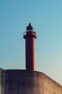 Low angle view of lighthouse against building against clear blue sky