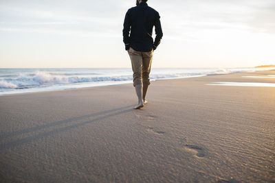 Low section of man walking at beach against sky