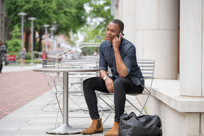 Full length of young man using phone while sitting on seat