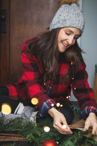 Smiling woman making wreath while sitting at home during christmas