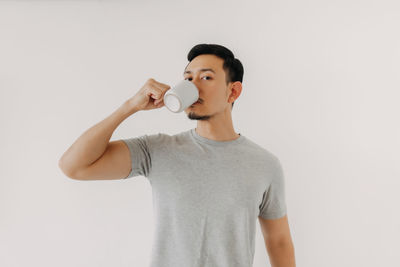 Full length of young man drinking glass against white background