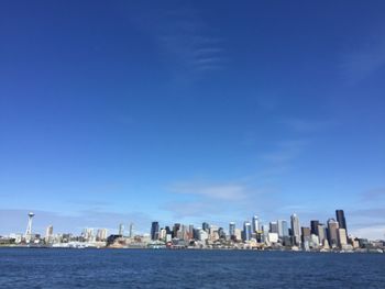 Sea by modern buildings against blue sky