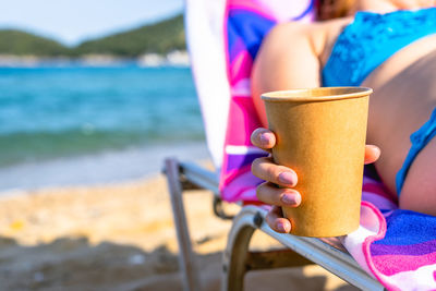 Close-up of woman holding disposable cup at beach