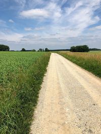 Dirt road amidst field against sky