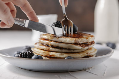 Woman cutting a slice of pancakes with knife and fork