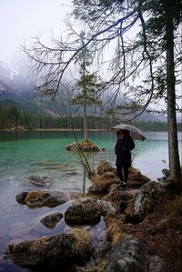 Young woman standing on rock by lake against sky