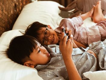 Siblings looking at mobile phone on bed