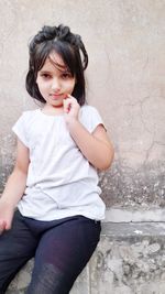 Portrait of cute girl sitting against wall