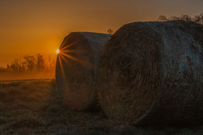 Hay bales on field against sky during sunset