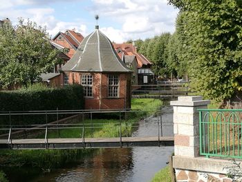 House by lake and buildings against sky