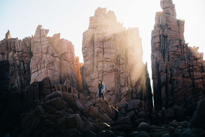Low angle view of man standing on rock against clear sky