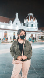 Young woman wearing flu mask looking away while standing outdoors