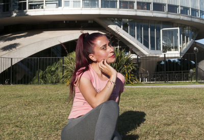 Happy woman sitting on grass against building