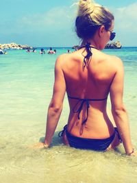 Rear view of sensuous woman in bikini sitting on shore