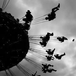 Low angle view of people enjoying on chain swing ride against sky