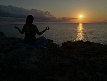 Side view of woman doing yoga at beach against sky during sunset
