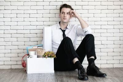 Portrait of a young man sitting against wall