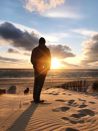 Rear view of man standing on beach against sky during sunset