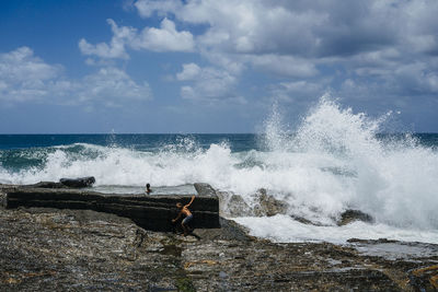 Sea waves splashing on rocky shore against sky