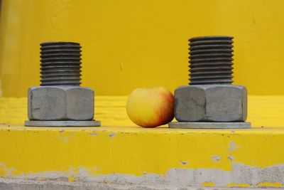 Apple amidst nut and bolt against yellow wall