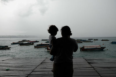 Rear view of women standing on sea against sky