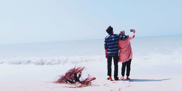 Couple taking selfie at beach against clear sky