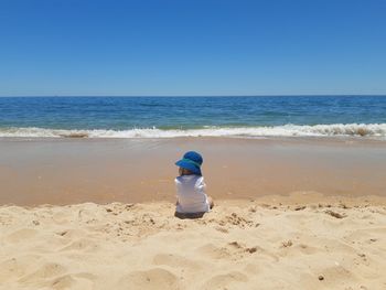 Back view of baby on beach against sky