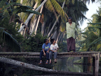 Man talking with boys sitting on footbridge over river