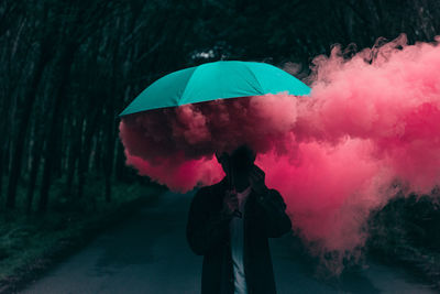 Man holding umbrella while standing with smoke on road in city