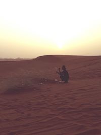 Silhouette man sitting on shore against clear sky during sunset