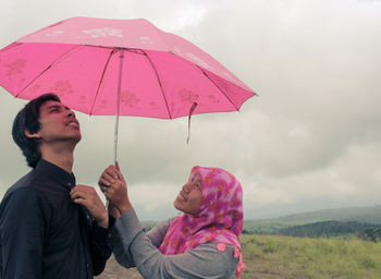 Young man with woman holding umbrella against sky during rainy season