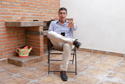 Full length of man sitting on chair against wall