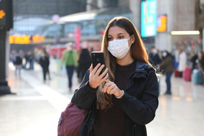 Young woman using phone while standing on land in city