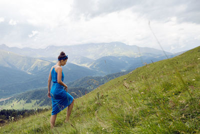 Woman in blue long dress standing on a high mountain in a meadow on a background of sheep